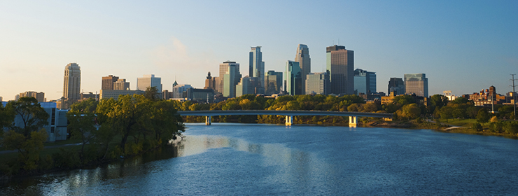 Downtown Minneapolis skyline in the Morning with a bridge midway and the Mississippi River in the foreground.